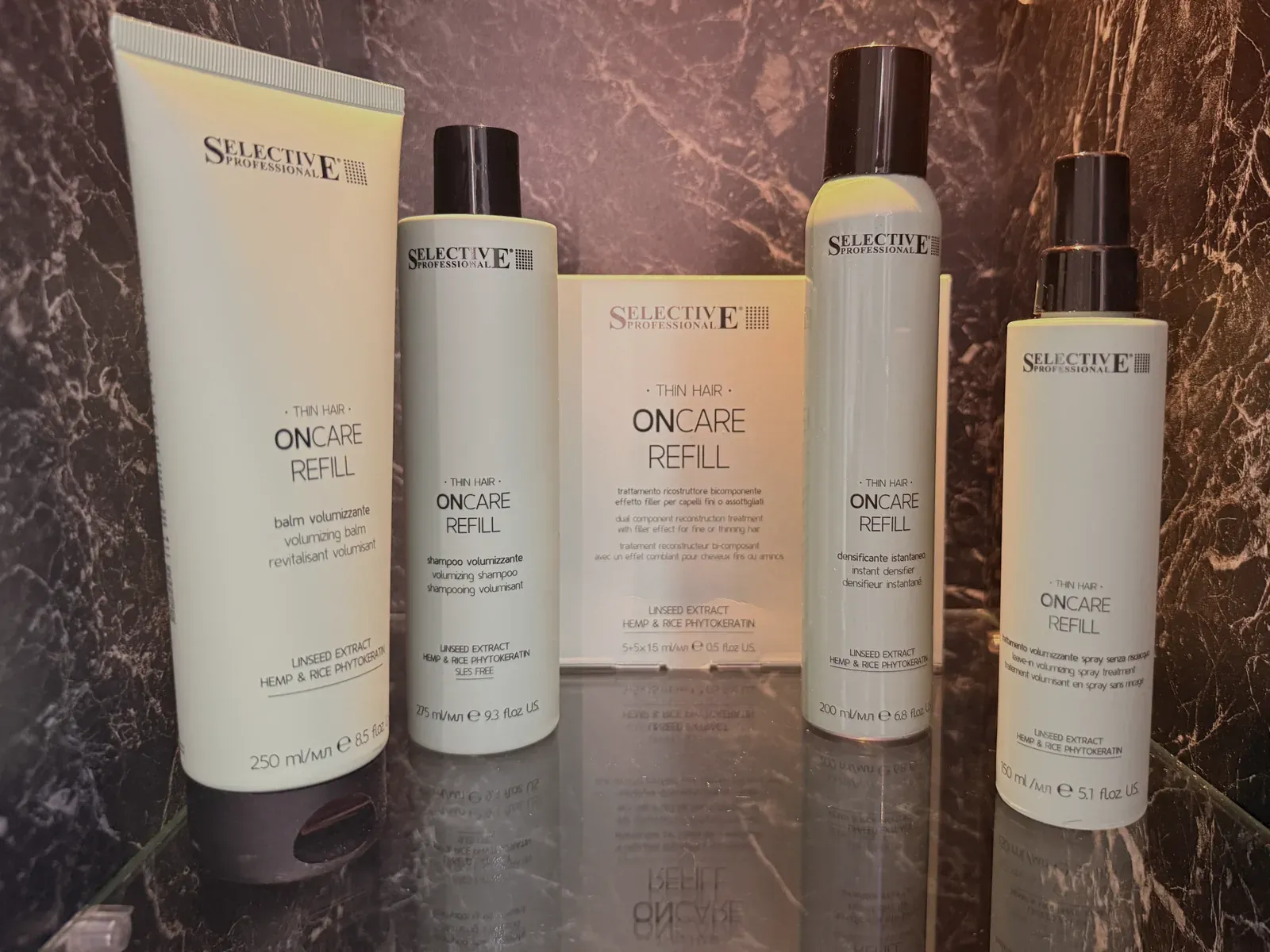 Die OnCare-Refill-Serie im Regal des Salons: Balm, Shampoo, Ampullen-Kur, Instant Densifier und Leave-in-Spray vor dunklem Marmor